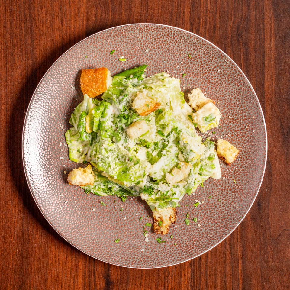 Top-down view of creamy Caesar salad with romaine lettuce, croutons, and grated cheese on a textured plate.