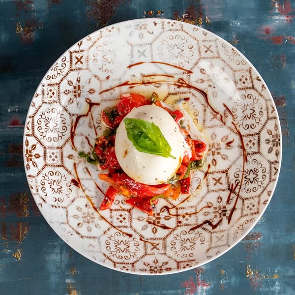 Burrata cheese with roasted red peppers, basil, and balsamic glaze on a decorative plate.