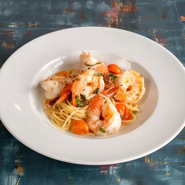 Shrimp scampi with spaghetti, cherry tomatoes, and fresh herbs in a white bowl.