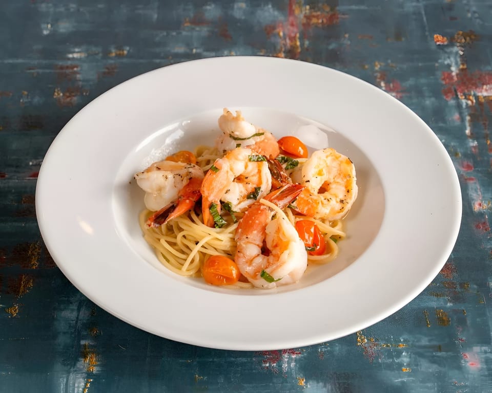 Shrimp scampi with spaghetti, cherry tomatoes, and fresh herbs in a white bowl.