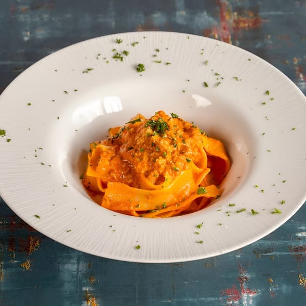 Pappardelle pasta with a rich red sauce and fresh parsley in a white bowl.