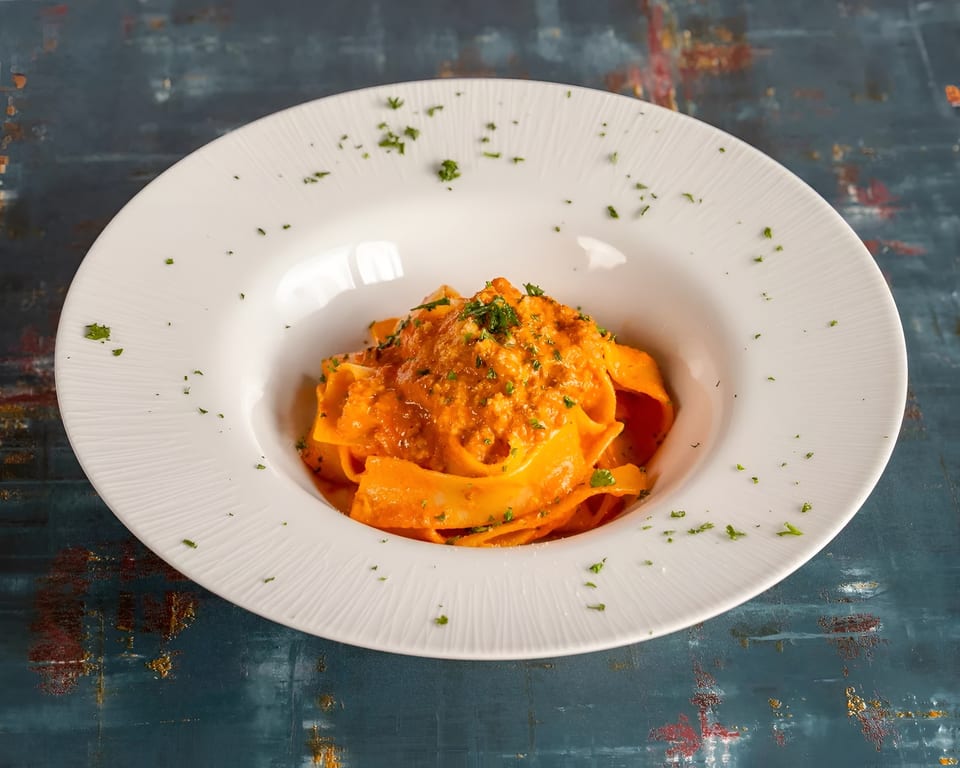 Pappardelle pasta with a rich red sauce and fresh parsley in a white bowl.