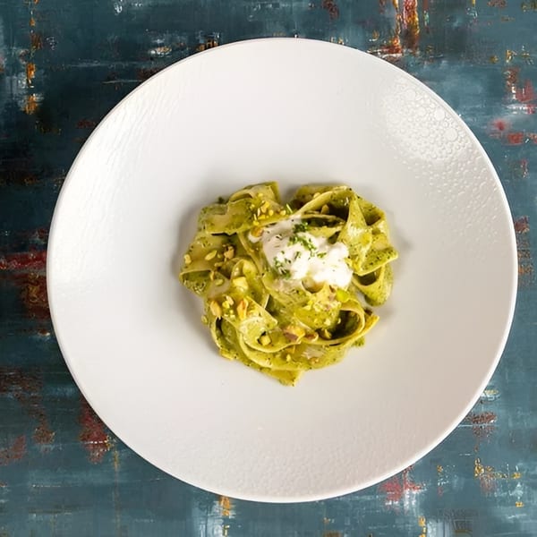 Green pasta with white sauce and chopped nuts on a white plate.
