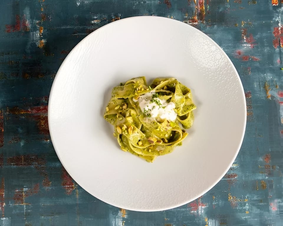 Green pasta with white sauce and chopped nuts on a white plate.