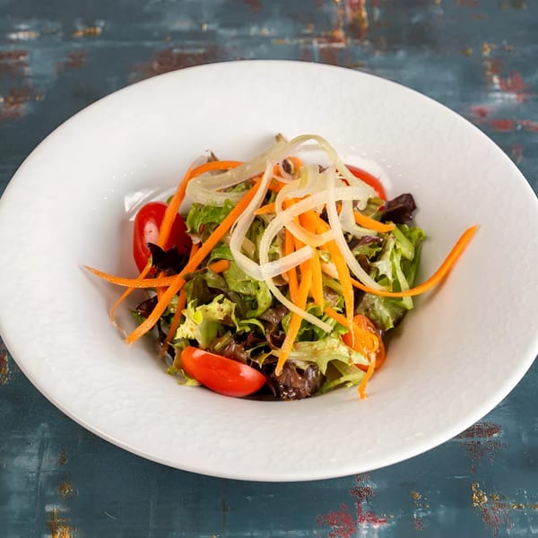 Fresh green salad with cherry tomatoes, shredded carrots, and onions in a white bowl.