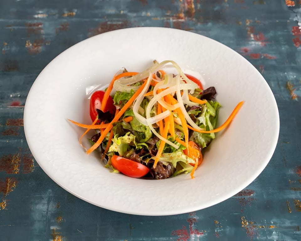 Fresh green salad with cherry tomatoes, shredded carrots, and onions in a white bowl.