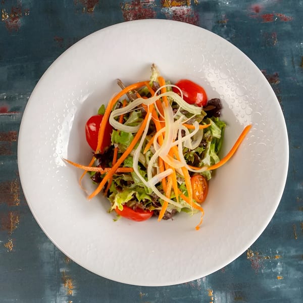 Fresh garden salad with mixed greens, cherry tomatoes, shredded carrots, and onions in a white bowl.