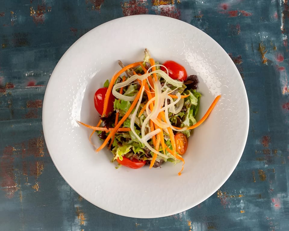 Fresh garden salad with mixed greens, cherry tomatoes, shredded carrots, and onions in a white bowl.