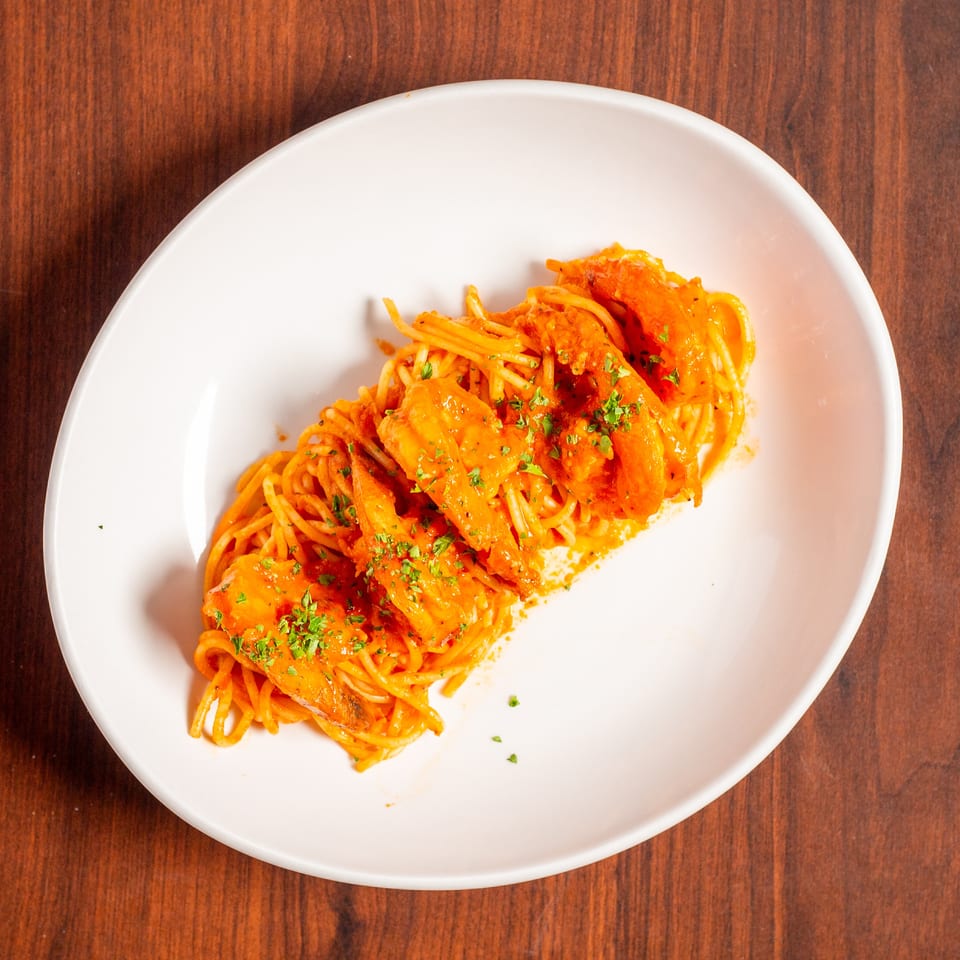 Spaghetti topped with orange sauce, grilled shrimp, and chopped herbs on a white plate over a wooden table.