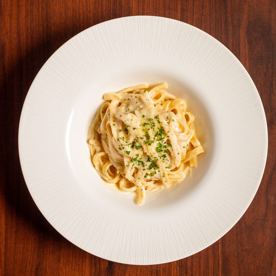 Creamy fettuccine Alfredo topped with grated cheese and parsley, served on a white plate over a wooden table.