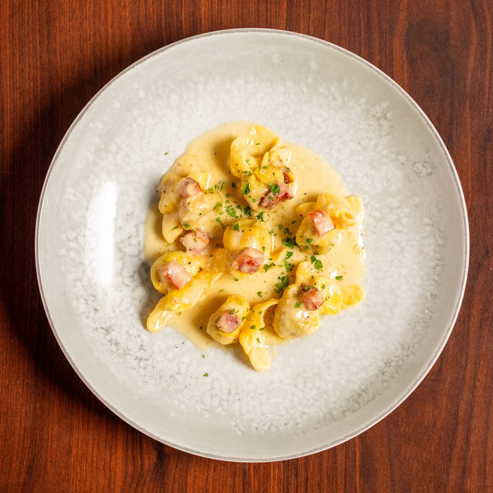 Creamy tortellini pasta with diced bacon and parsley served on a white plate atop a wooden table.