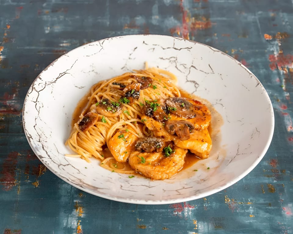 Chicken and mushroom pasta with a creamy sauce, garnished with parsley, served in a white bowl.