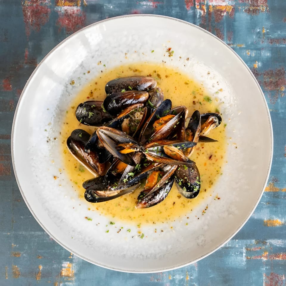 Steamed mussels in a creamy broth, garnished with fresh herbs, served in a white bowl.