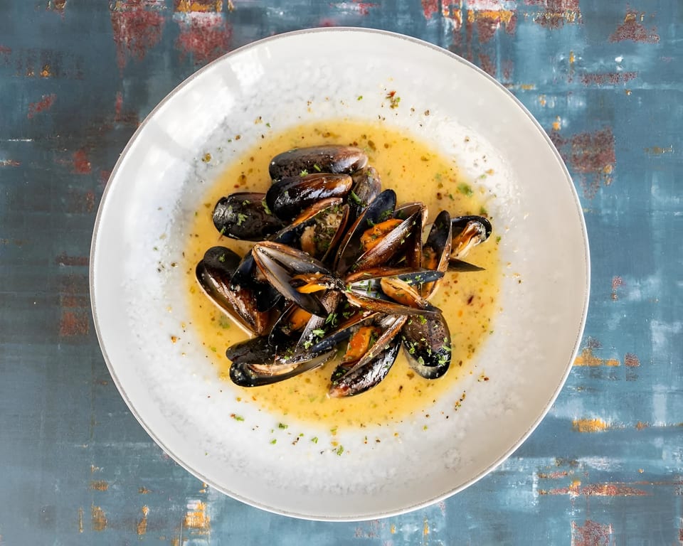 Steamed mussels in a creamy broth, garnished with fresh herbs, served in a white bowl.