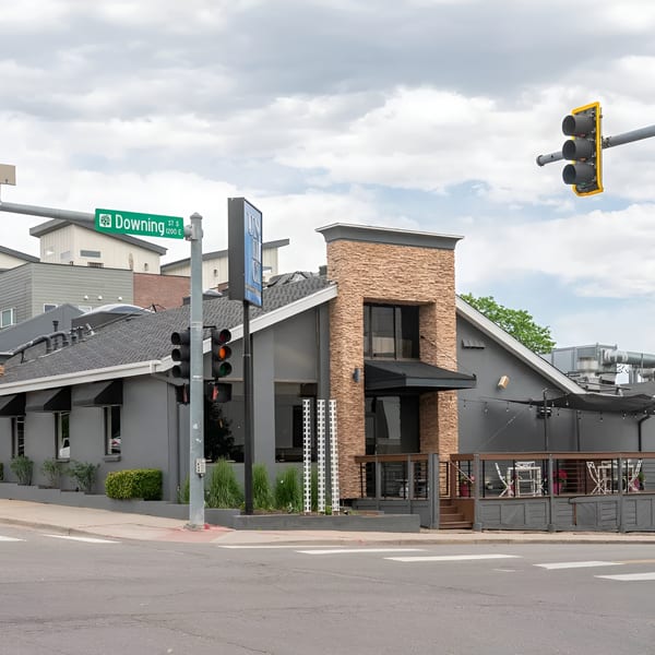 Exterior view of Ondici restaurant, a gray building with stone accents and an outdoor patio, on a street corner.