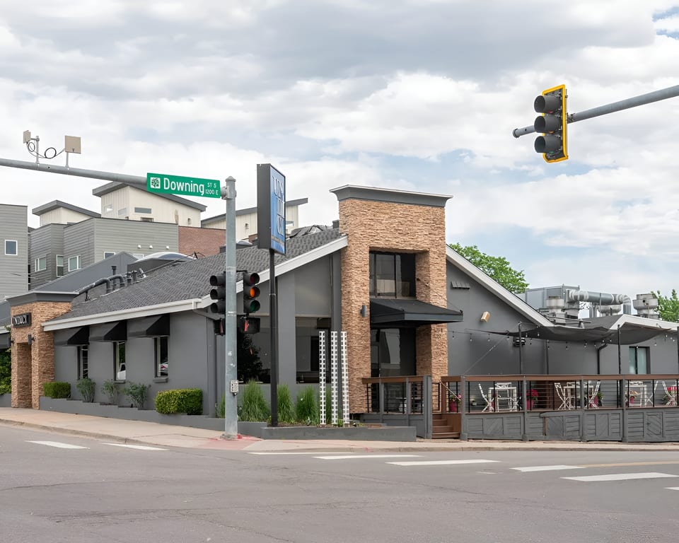 Exterior view of Ondici restaurant, a gray building with stone accents and an outdoor patio, on a street corner.