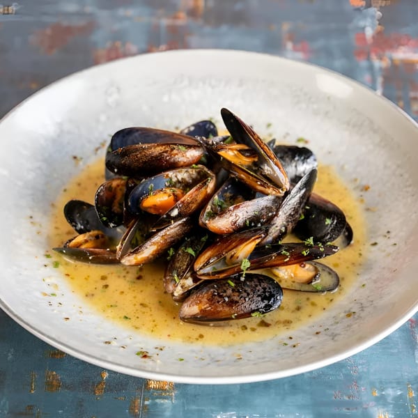 Steamed mussels in a creamy broth, garnished with fresh herbs, served on a white plate.