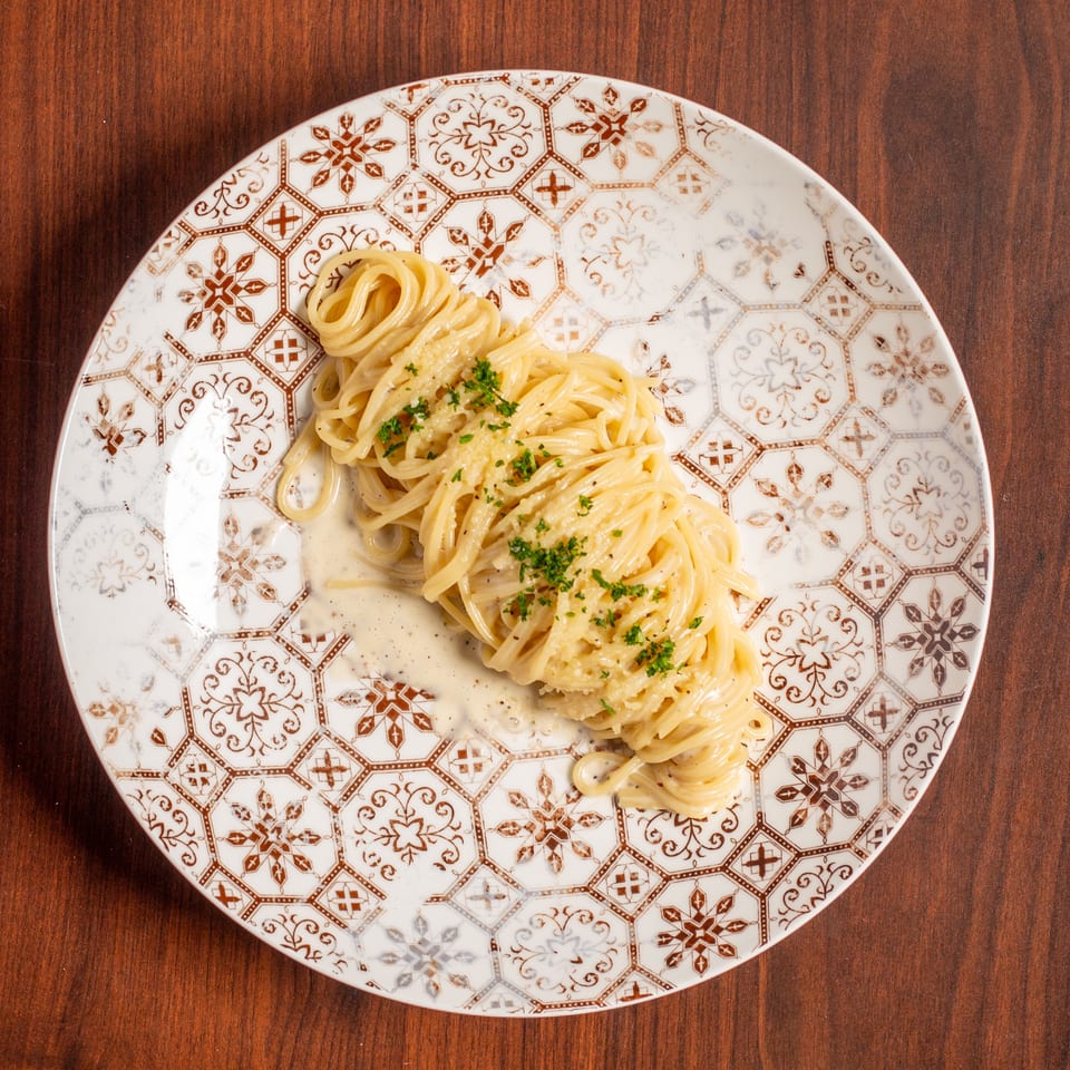 Creamy linguine topped with grated cheese and parsley on an ornate patterned plate atop a wooden table.