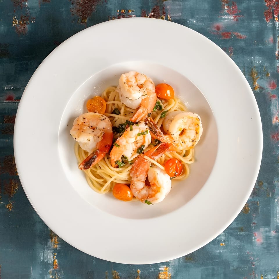 Shrimp scampi with spaghetti, cherry tomatoes, and herbs in a white bowl.