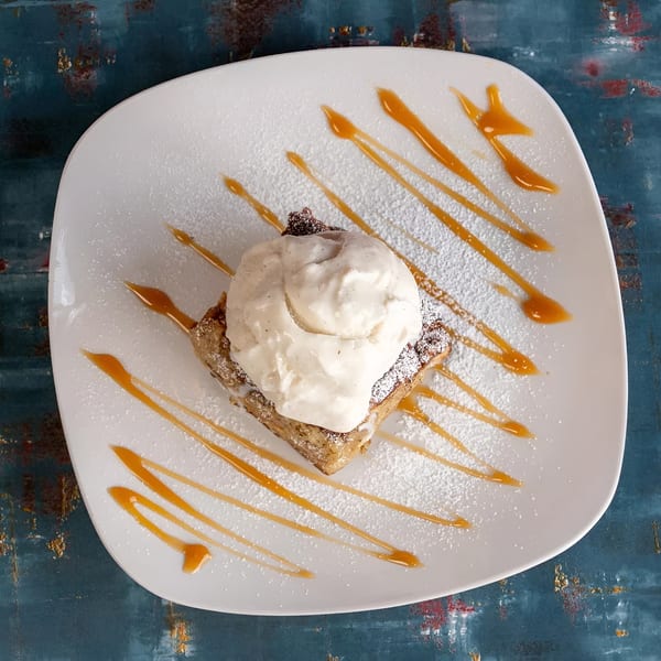 Dessert on a white plate with a scoop of vanilla ice cream, caramel drizzle, and powdered sugar.