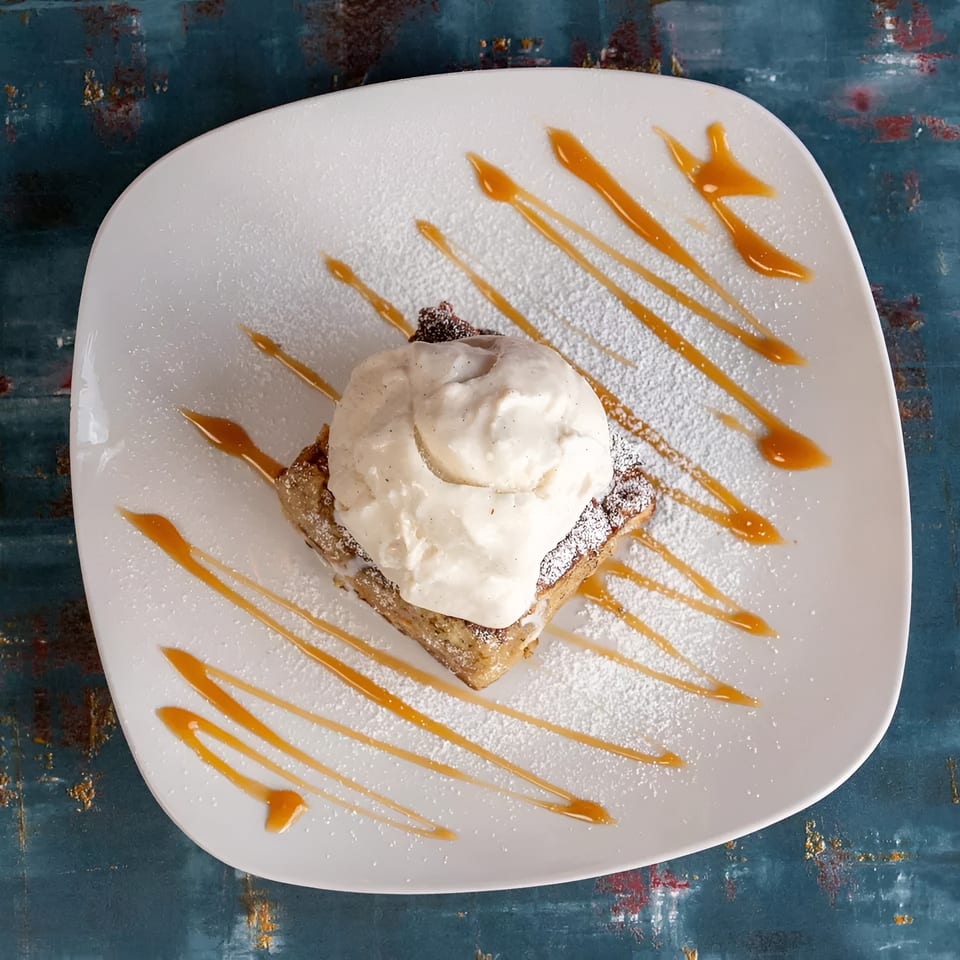 Dessert on a white plate with a scoop of vanilla ice cream, caramel drizzle, and powdered sugar.