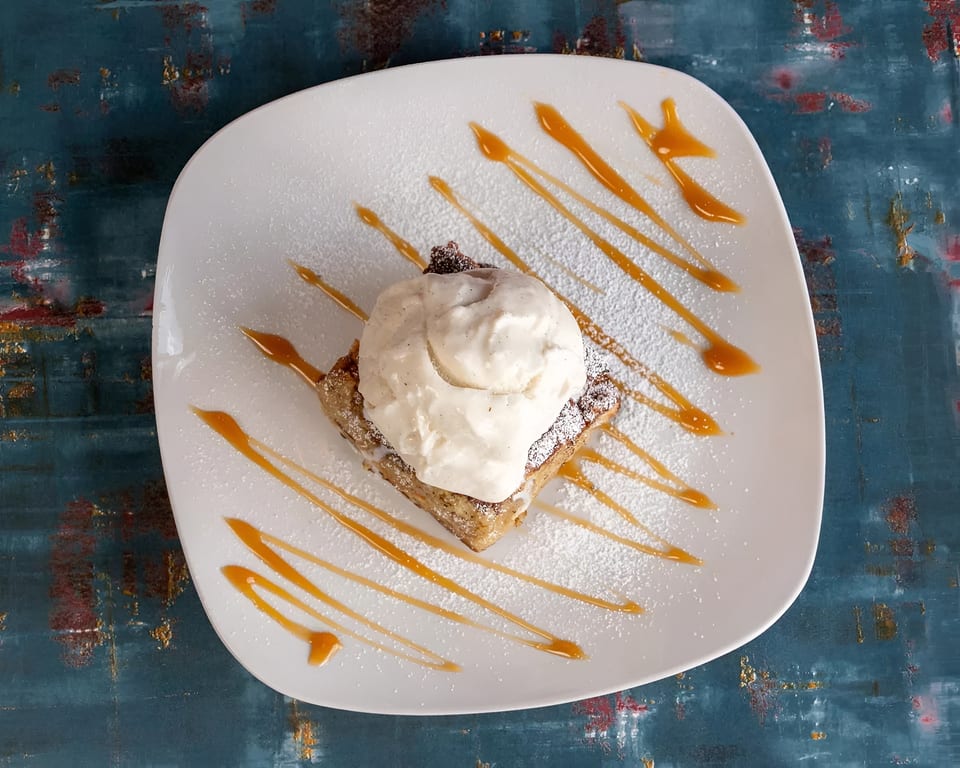 Dessert on a white plate with a scoop of vanilla ice cream, caramel drizzle, and powdered sugar.