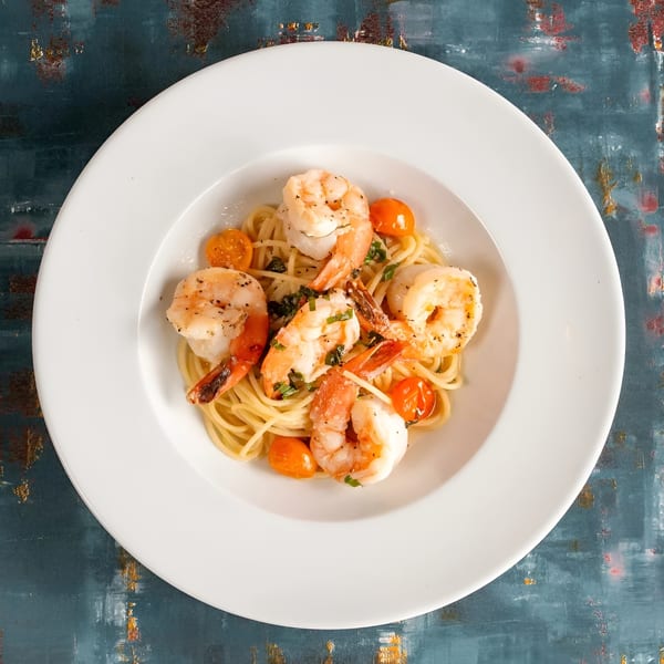 Shrimp scampi with spaghetti, cherry tomatoes, and herbs in a white bowl.