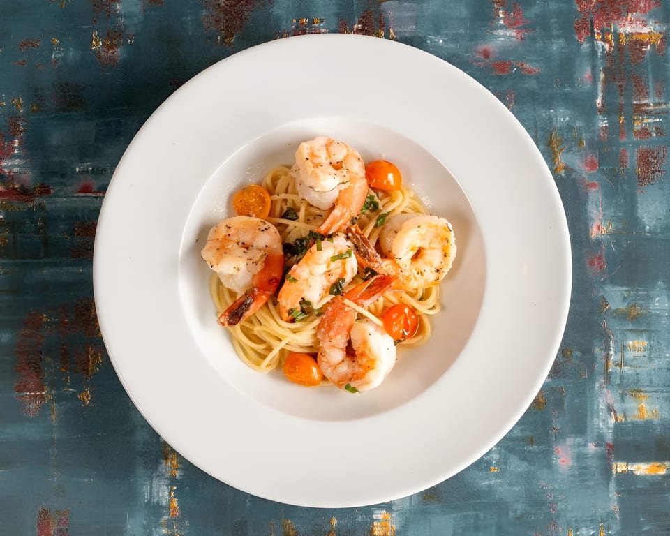 Shrimp scampi with spaghetti, cherry tomatoes, and herbs in a white bowl.